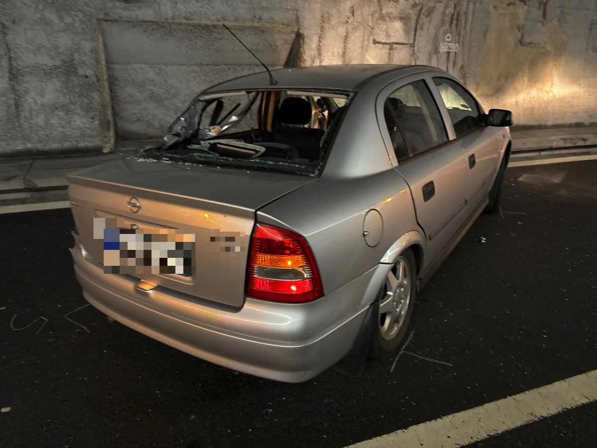 Ein silberfarbenes Auto der Marke Opel steht mit beschädigter Heckscheibe auf einer Straße. Der Wagen befindet sich nahe einer Tunnelwand.