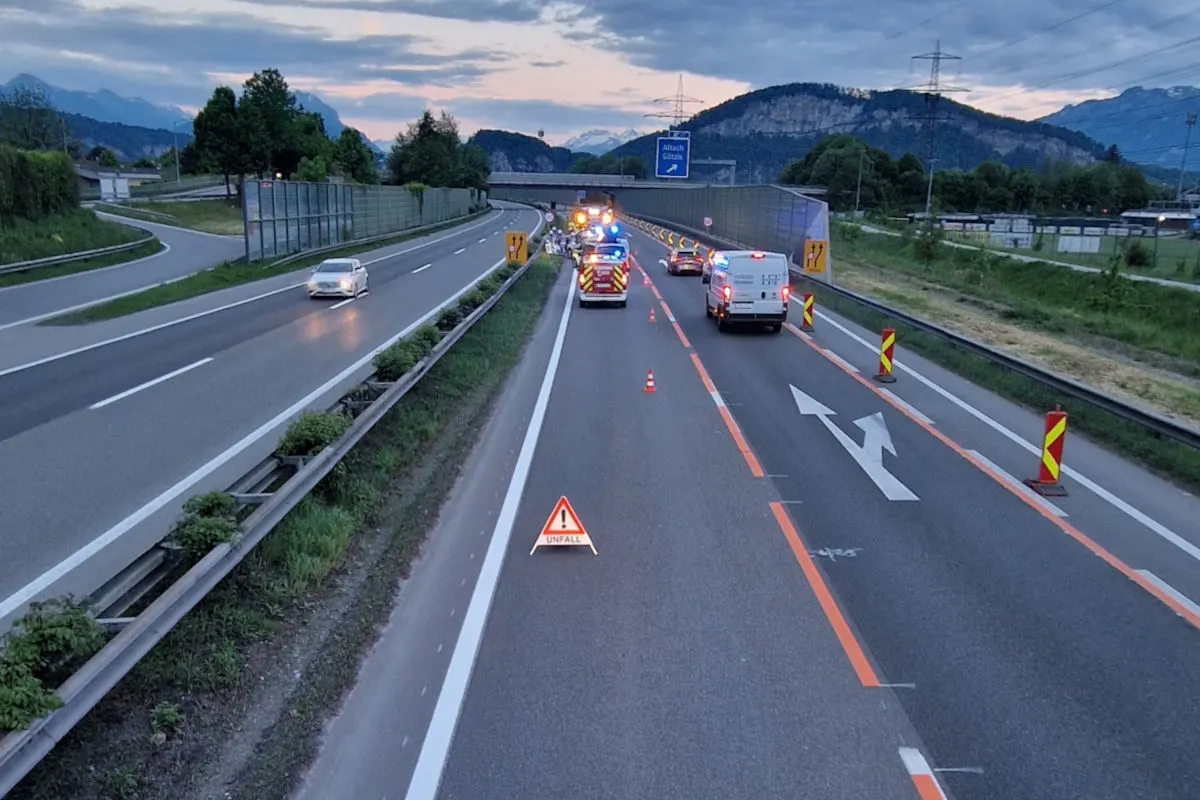 Eine Autobahn bei Dämmerung zeigt Einsatzfahrzeuge mit blinkenden Lichtern und ein 'Unfall' Warnschild auf der Fahrbahn.