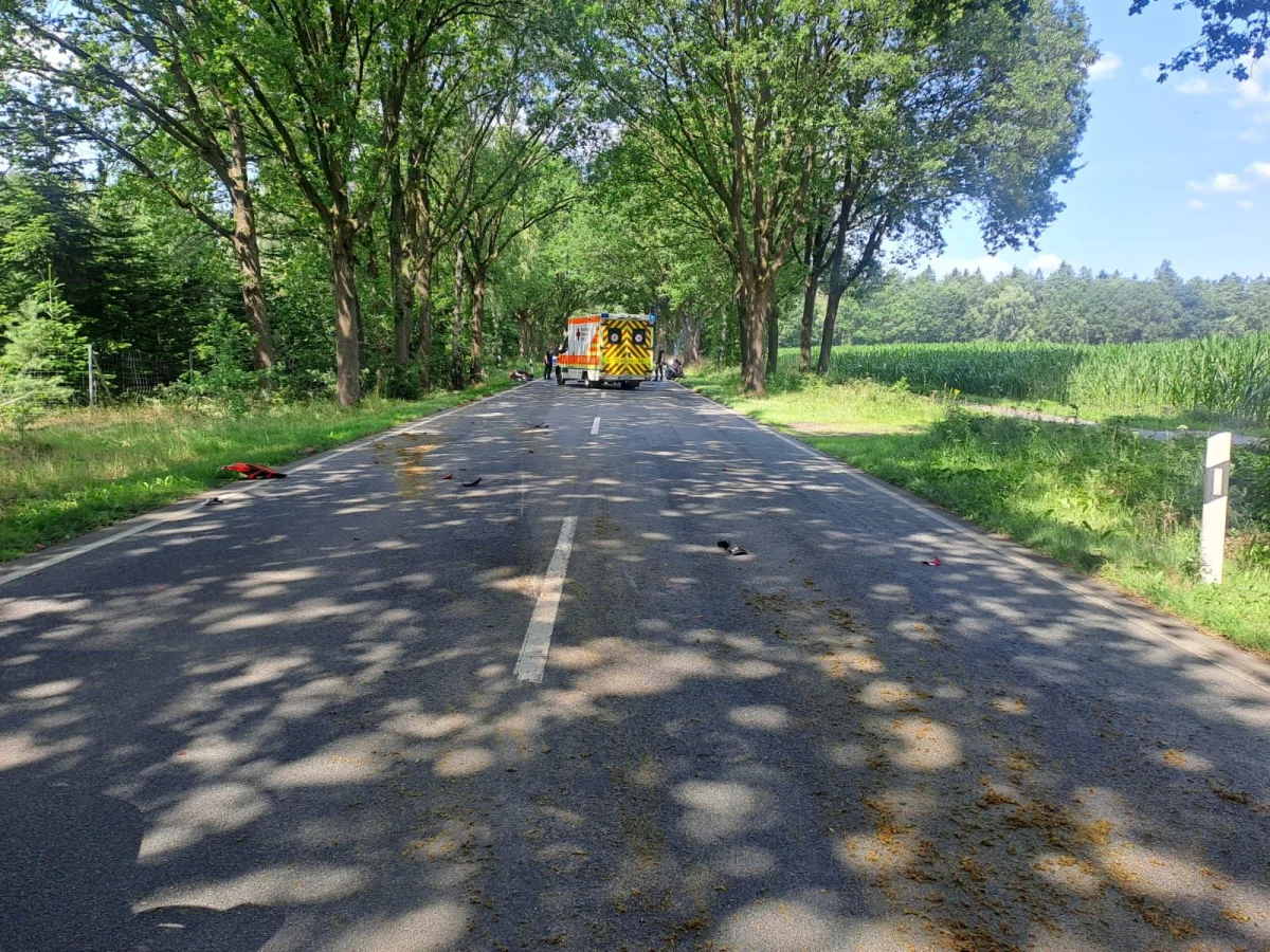 Ein Rettungsfahrzeug steht auf einer geraden, von Bäumen gesäumten Landstraße. Die Umgebung ist grün und bewaldet.