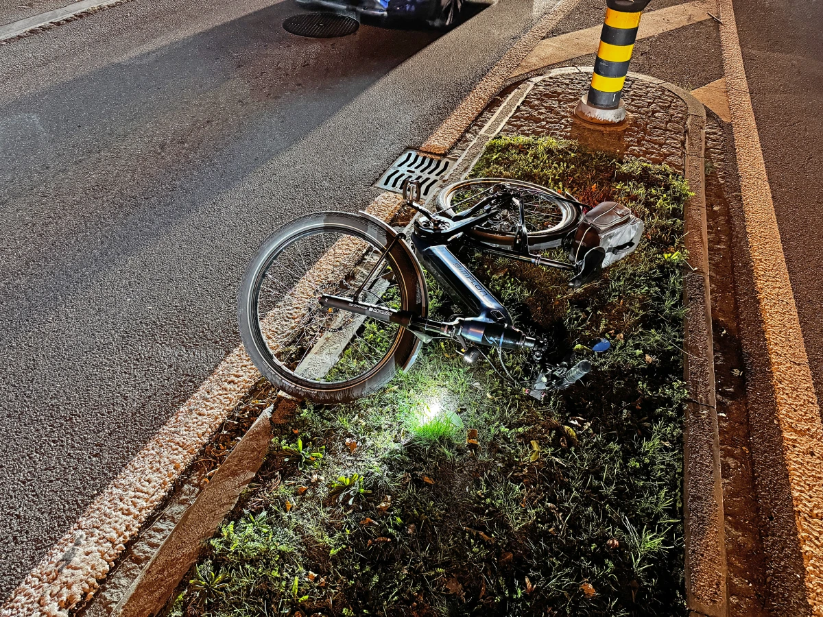 Ein unbeschädigtes Fahrrad liegt auf einem Mittelstreifen mit Gras und Kies, während es Nacht ist und Straßenbeleuchtung die Szene dämpft.