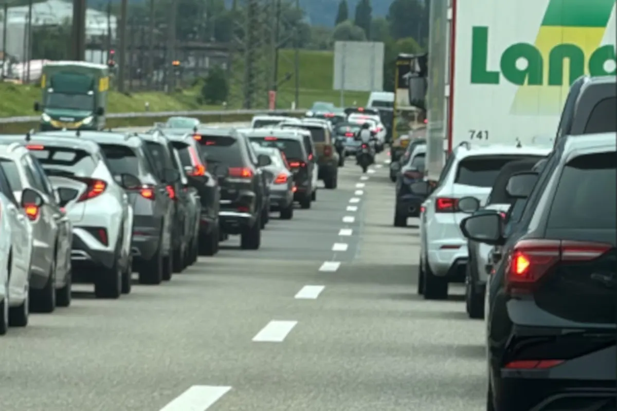 Auf einer Autobahn stauen sich zahlreiche Autos und ein großer Lastwagen, während der Verkehr stockt. Die Fahrzeuge stehen dicht hintereinander, sichtbar in beiden Fahrspuren.