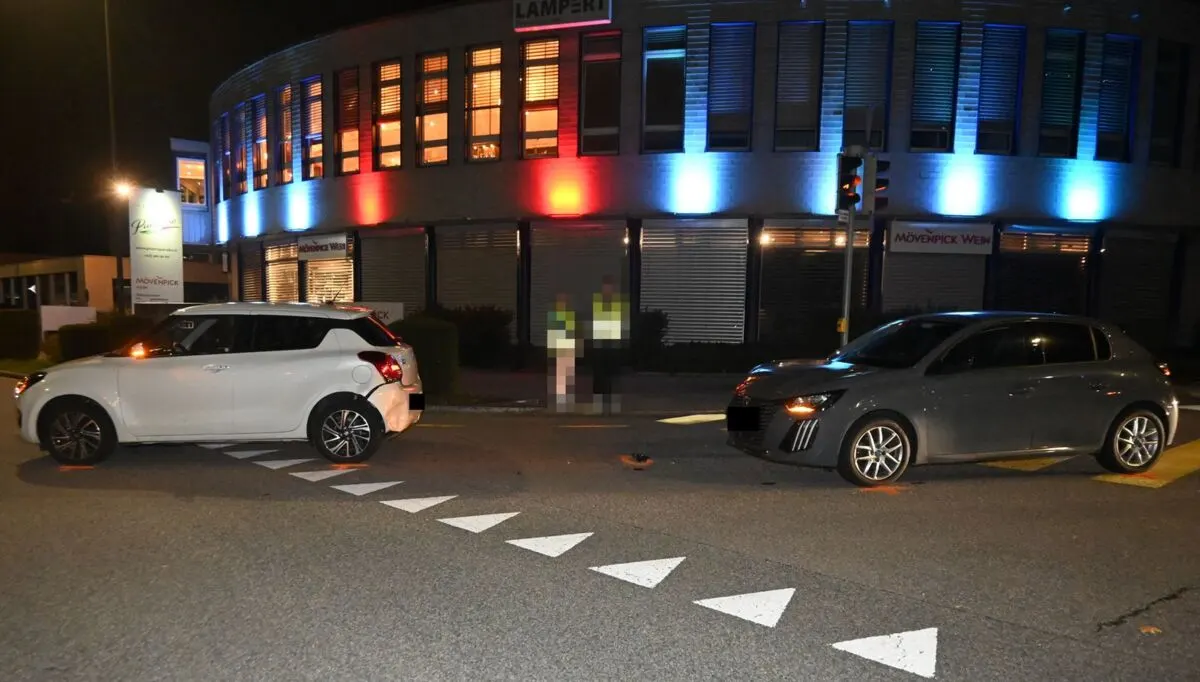 Zwei Autos stehen an einer Kreuzung in der Nacht. Im Hintergrund ist ein beleuchtetes Gebäude zu sehen.