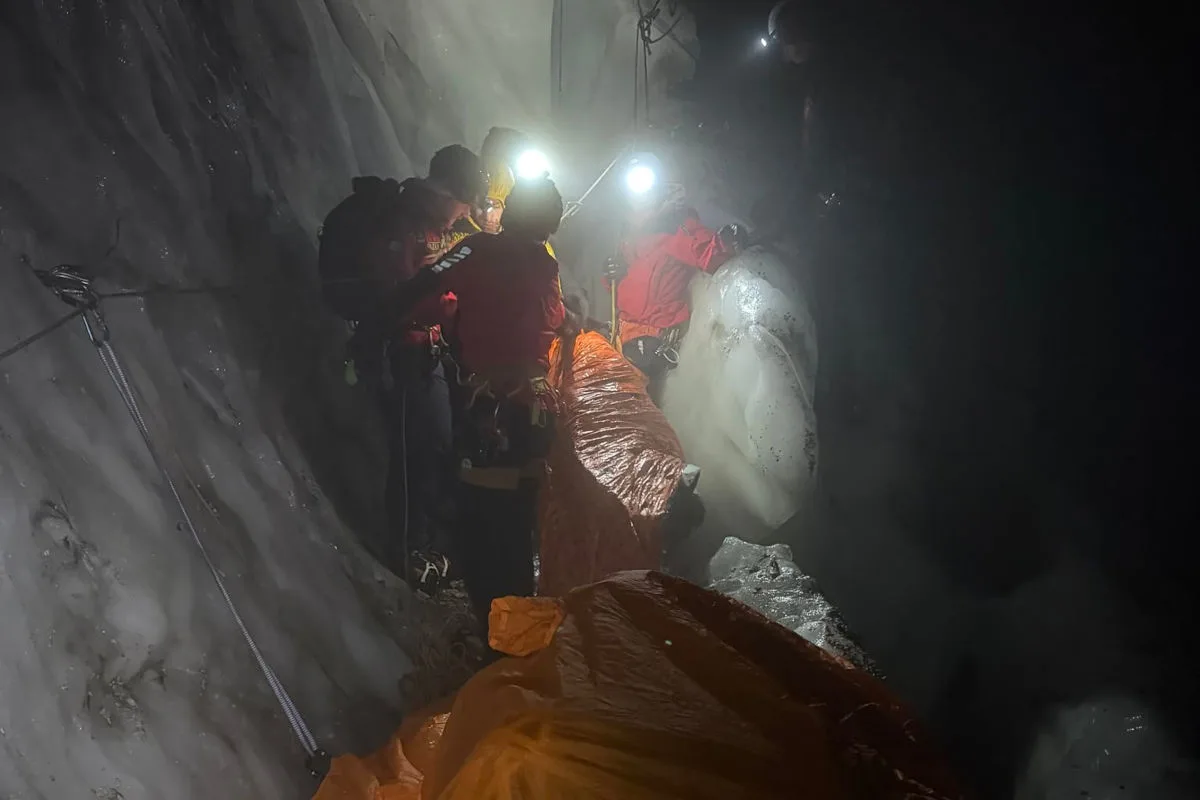 Mehrere Rettungskräfte sind in einer dunklen, vereisten Schlucht bei Nacht im Einsatz. Sie tragen Lampen und verwenden Ausrüstung, um jemandem zu helfen.