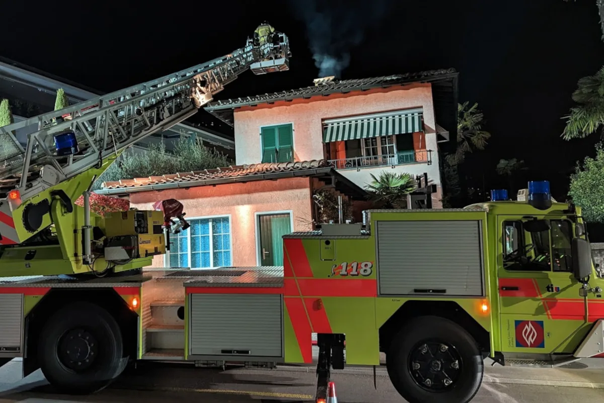 Eine Feuerwehrleiter ist ausgefahren zu einem Hausdach, aus dem Rauch aufsteigt. Das Bild zeigt einen Einsatz in der Nacht.
