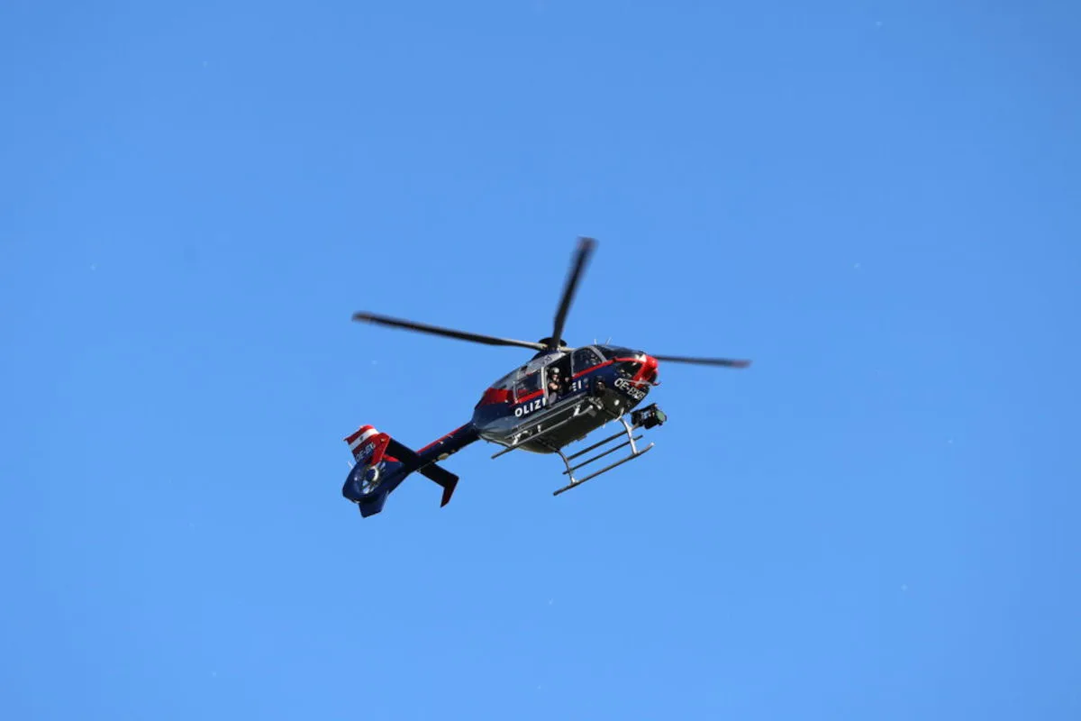 Ein Polizeihubschrauber mit Erkennungsmarken fliegt hoch am blauen Himmel. Die Rotoren sind in Bewegung.
