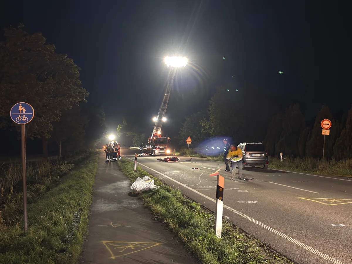 Auf einer Landstraße bei Nacht sichern Einsatzkräfte eine Unfallstelle. Ein Fahrzeug steht am rechten Fahrbahnrand, während Scheinwerfer die Szene erhellen.
