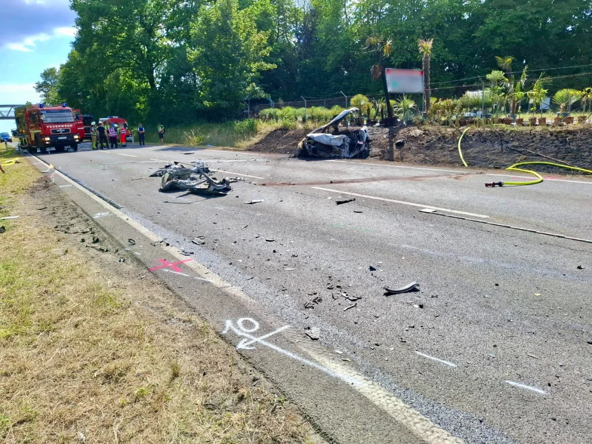 Ein stark beschädigtes Auto steht abseits der Straße, während Feuerwehrleute am Einsatzort arbeiten. Trümmer sind über die Fahrbahn verstreut.