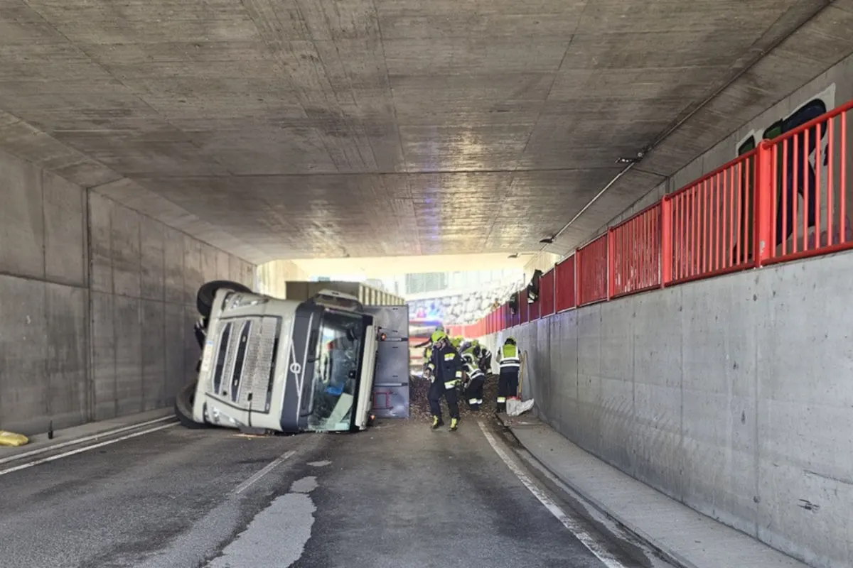 Ein umgekippter Lastwagen liegt auf der Seite in einer engen Unterführung. Feuerwehrleute in gelben Helmen sind im Einsatz.