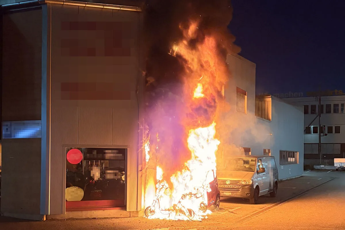 Ein Fahrzeug steht in Flammen neben einem Gebäude. Der Brand erzeugt dichten Rauch in der Umgebung.