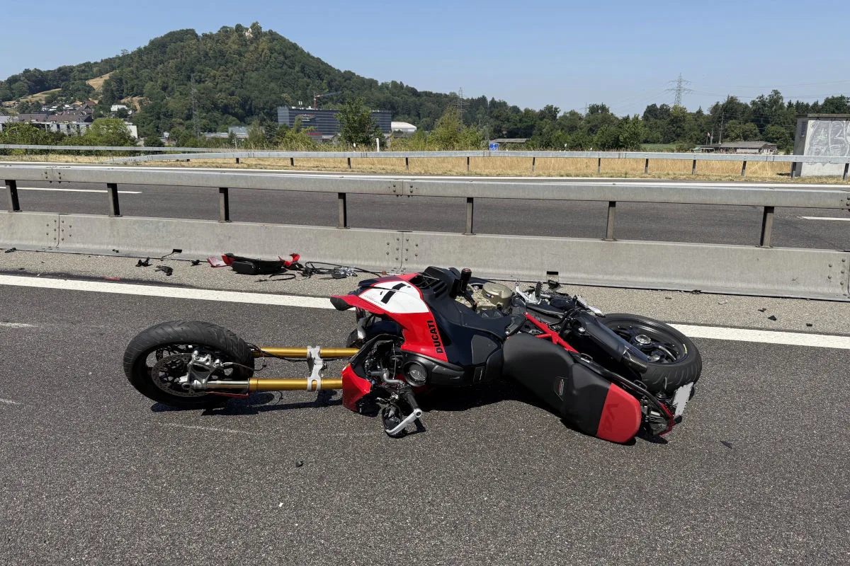 Ein rotes Ducati-Motorrad liegt nach einem Unfall auf der Autobahn. Im Hintergrund sind Hügel und eine Leitplanke zu sehen.