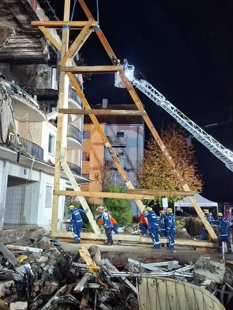 THW-Mitarbeiter arbeiten nachts an der Sicherung eines stark beschädigten Gebäudes mit einer Holzkonstruktion. Trümmer liegen am Boden.