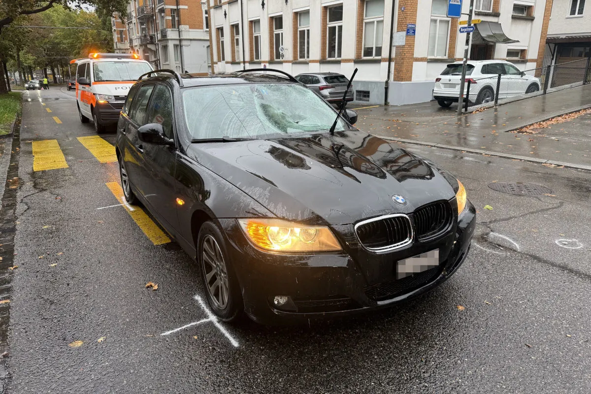 Ein schwarzer BMW steht mit beschädigter Windschutzscheibe auf einer regennassen Straße. Im Hintergrund ist ein Polizeifahrzeug zu sehen.
