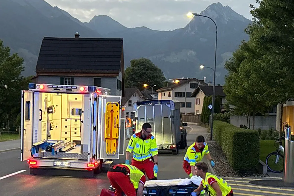 Ein Rettungsteam kümmert sich um eine Trage auf einer Dorfstraße. Ein geöffneter Krankenwagen steht im Hintergrund bereit.