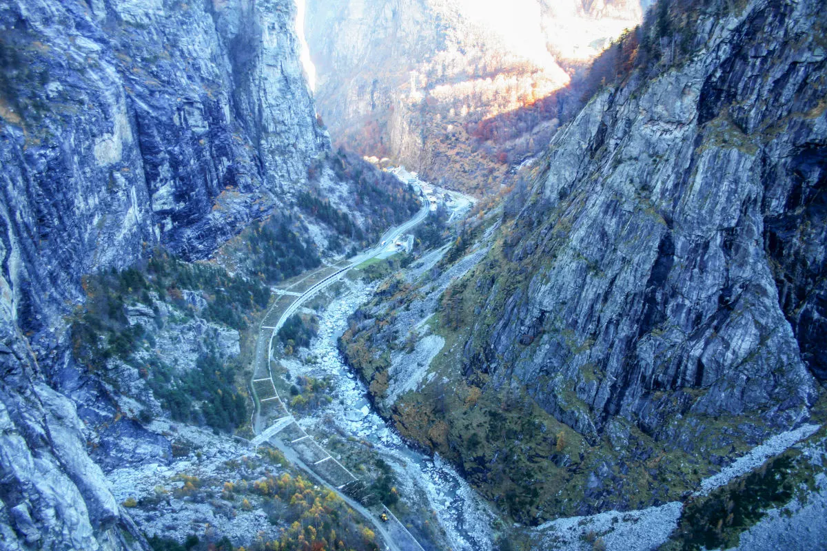 In einem steilen Gebirgstal verläuft eine gewundene Straße entlang der felsigen Klippen. Die Umgebung ist von Bergen und herbstlicher Vegetation geprägt.