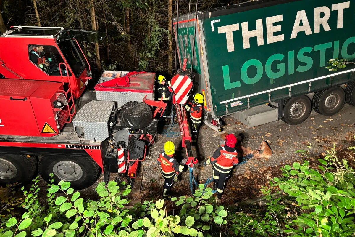 Ein roter Kran steht neben einem umgestürzten Lkw. Feuerwehrleute in Uniform arbeiten daran, den Lkw mit Seilen zu sichern.