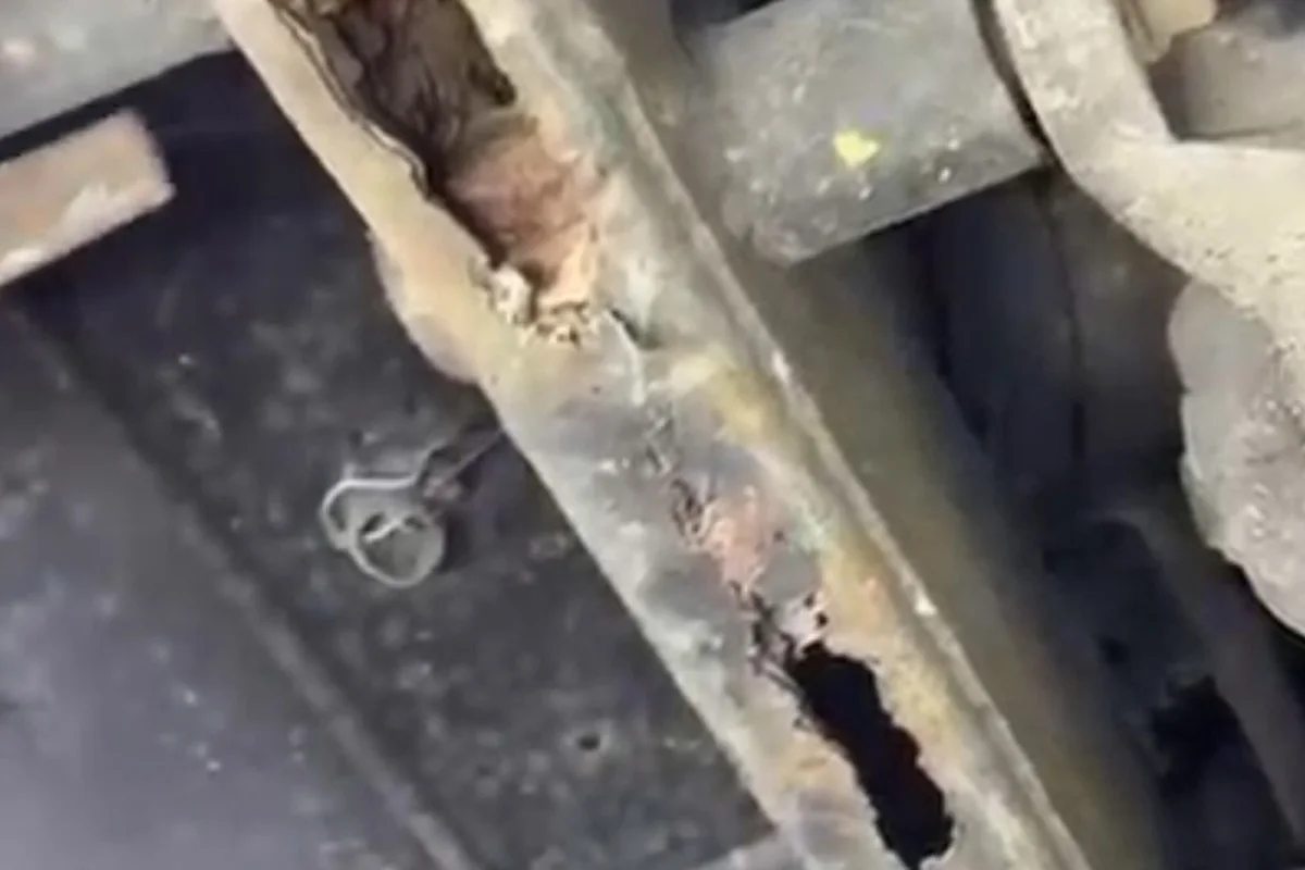 Zu sehen ist eine stark verrostete und durchlöcherte Metallstruktur unter einem Fahrzeug. Der Rost hat das Metall deutlich geschwächt.