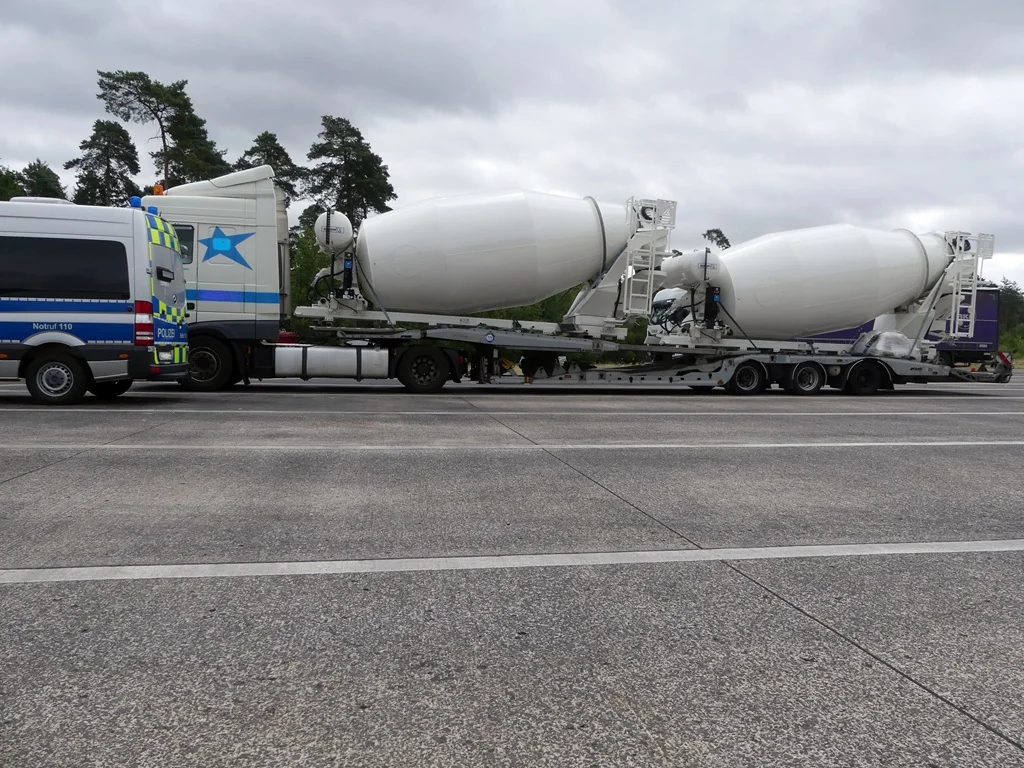 Ein Polizeifahrzeug steht neben einem Lkw mit zwei großen Betonmischern auf einer Autobahn. Der Himmel ist bewölkt.