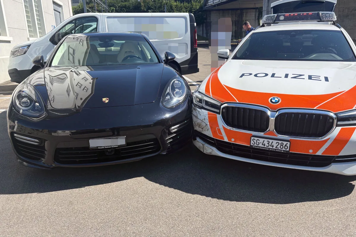 Ein Polizeifahrzeug der Kantonspolizei St. Gallen kollidiert leicht seitlich mit einem schwarzen Porsche auf einem Parkplatz. Im Hintergrund ist ein weißer Lieferwagen zu sehen.