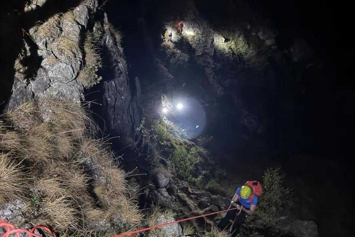 Ein Bergretter seilt sich bei Nacht an einer steilen Felswand ab. Im Hintergrund sind weitere Personen mit Taschenlampen zu erkennen.