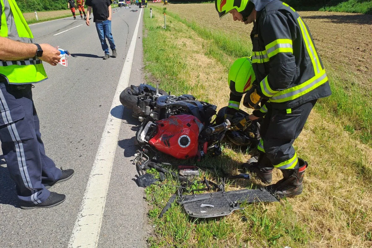 Auf einer Landstraße liegt ein umgekipptes Motorrad auf dem Grünstreifen, während ein Feuerwehrmann die Situation begutachtet. Ein weiterer Mann in Zivilkleidung steht daneben.