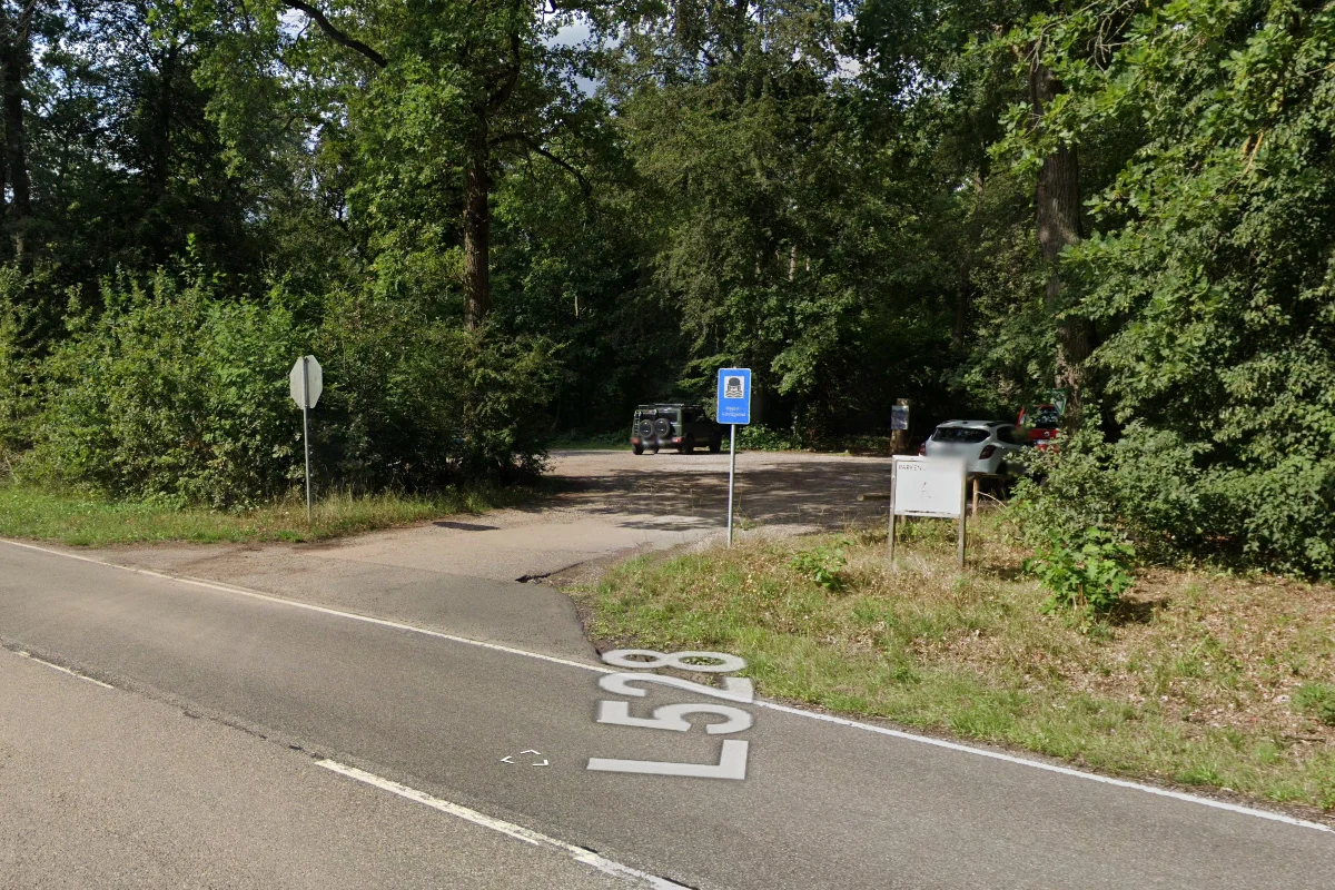 Ein Wegweiser und zwei Fahrzeuge sind auf einem Parkplatz neben der Landstraße L528 zu sehen, umgeben von Wald.