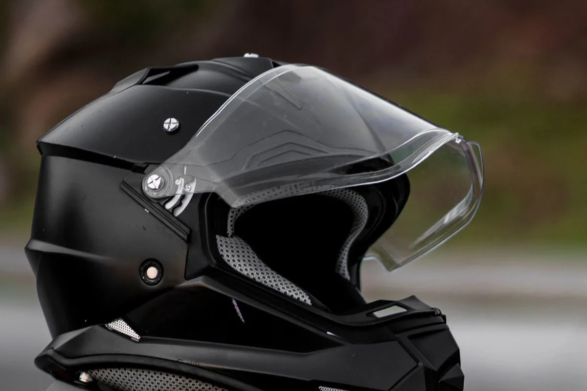 Ein schwarzer Motorradhelm mit einem transparenten, hochgeklappten Visier steht im Fokus des Bildes.