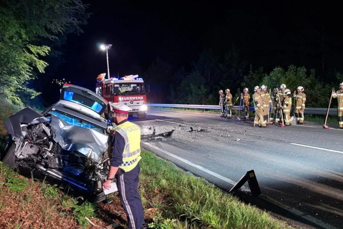 Ein stark beschädigtes Auto steht schräg am Straßenrand, während Polizisten und Feuerwehrkräfte bei Nacht die Unfallstelle sichern.