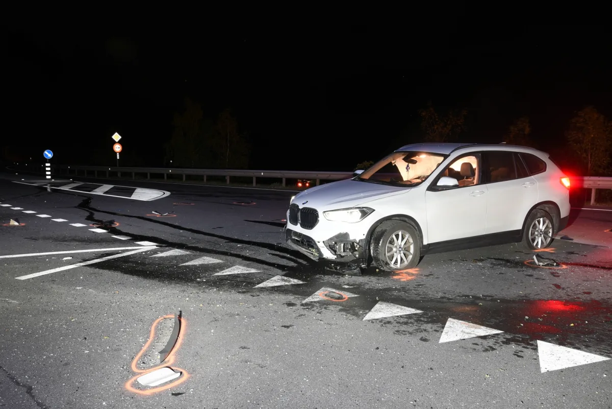 Ein weißer BMW SUV mit sichtbaren Frontschäden steht auf einer Straße. Es ist Nacht, und die Umgebung ist schwach beleuchtet.