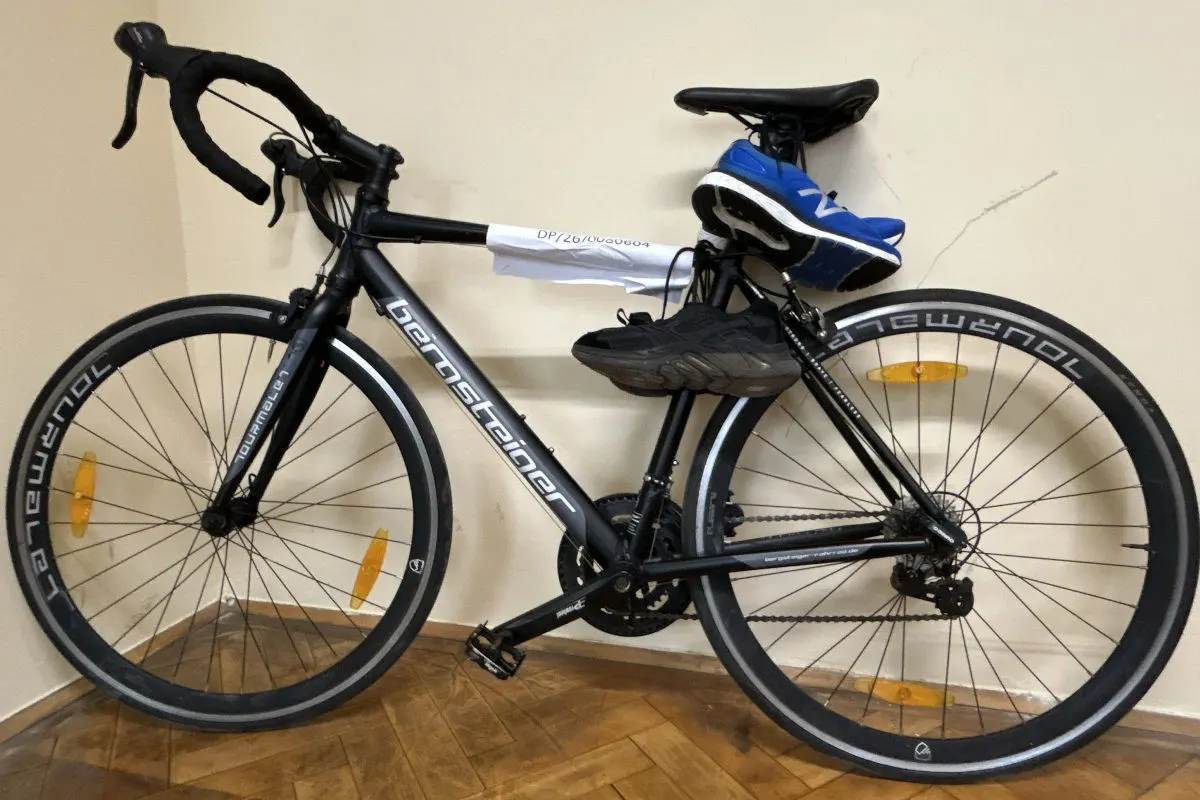 Ein schwarzes Fahrrad steht in einem Raum. Auf dem Sattel liegen zwei Paar Schuhe, ein blaues und ein schwarzes.