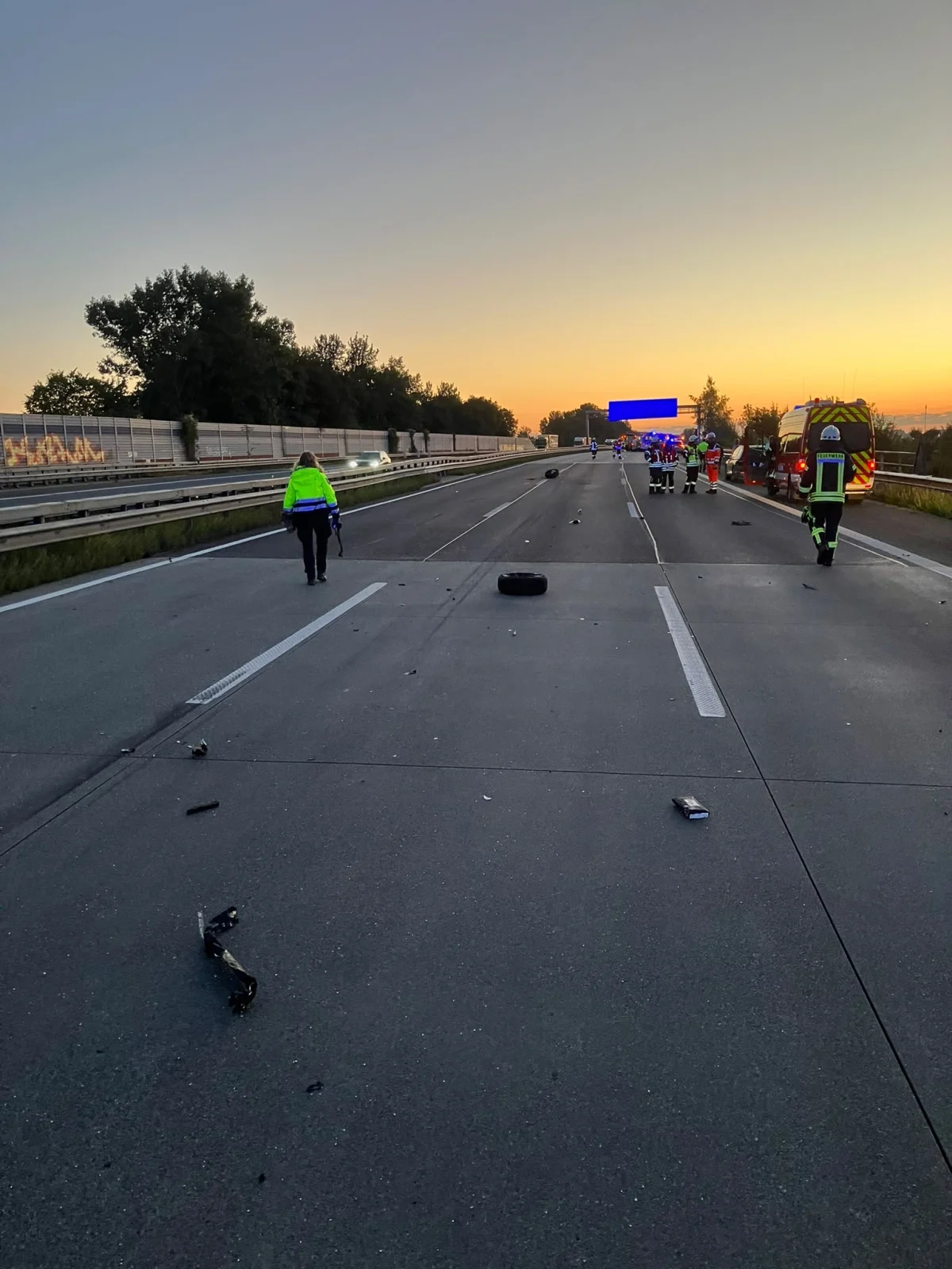 Auf einer Autobahn sind bei Sonnenuntergang Feuerwehrleute und Polizeikräfte im Einsatz. Trümmer sind auf der Fahrbahn verstreut.