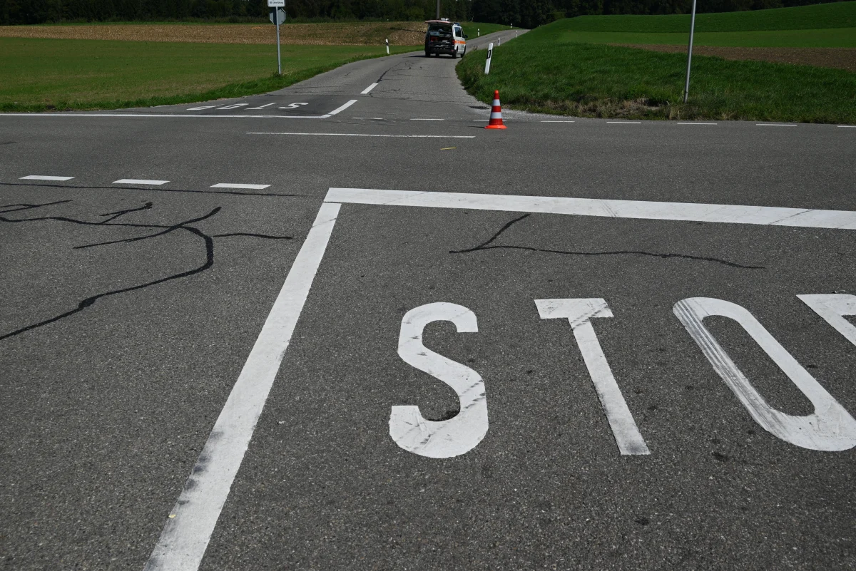 Eine ländliche Straßenkreuzung mit einer Stop-Malerei im Vordergrund und einem Fahrzeug in der Ferne.