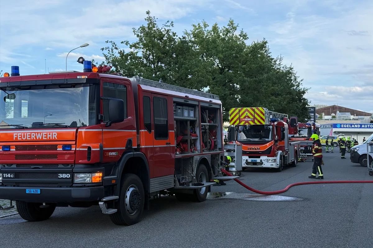 Mehrere Feuerwehrfahrzeuge sind auf einer Straße geparkt. Feuerwehrleute in Uniformen arbeiten mit angeschlossenen Wasserschläuchen.