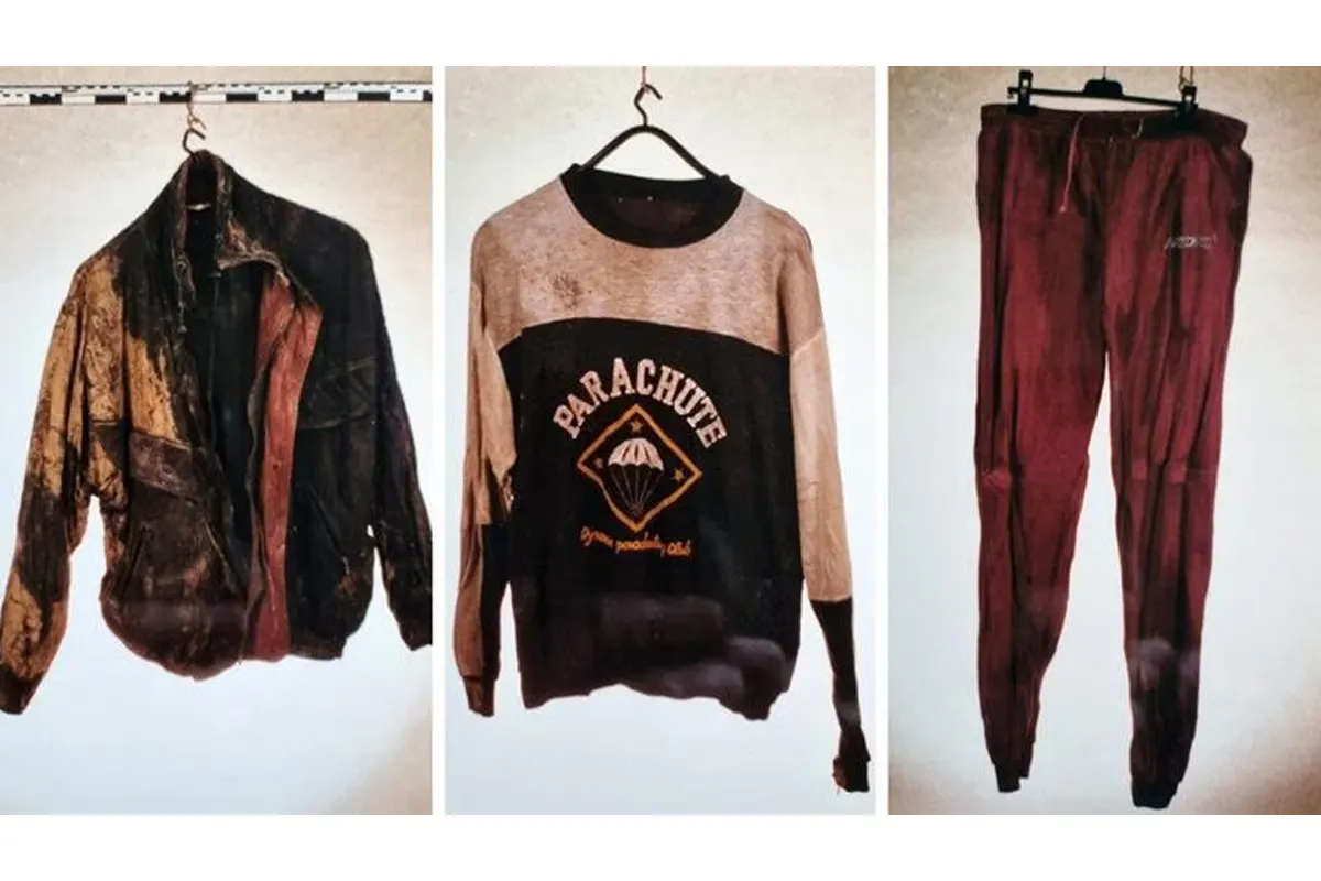Drei Kleidungsstücke hängen auf Bügeln: eine stark verschmutzte Jacke, ein Pullover mit 'Parachute'-Aufdruck und eine rote Hose.