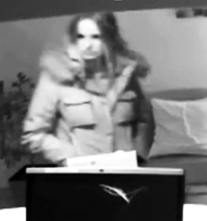 Eine unscharfe Aufnahme zeigt eine Person mit einem dicken Mantel in einem Innenraum, festgehalten von einer Überwachungskamera.