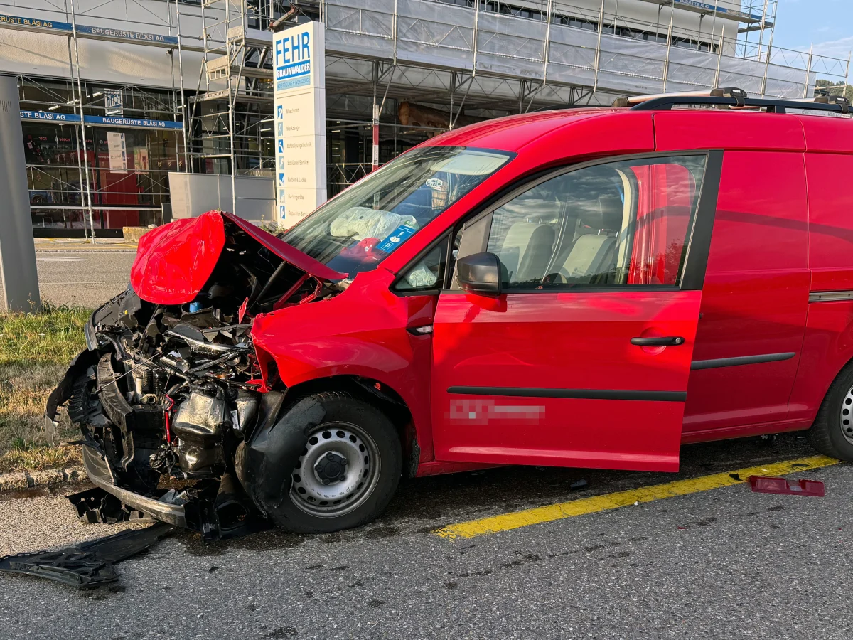 Ein roter Lieferwagen mit stark deformierter Front steht auf der Straße vor einem Gebäude. Der Unfall ereignete sich offenbar in einem Gewerbegebiet.