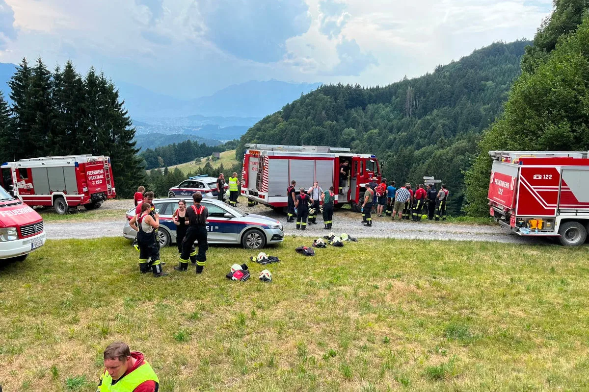 Mehrere Feuerwehrfahrzeuge und ein Polizeiauto stehen auf einer Wiese in bergigem Gelände. Feuerwehrkräfte sind in Aktion.
