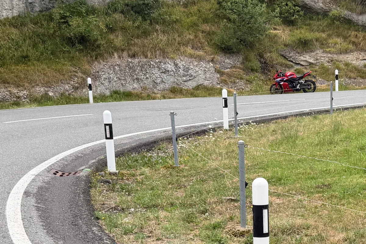 Ein rotes Motorrad ist auf einer kurvigen Landstrasse zu sehen. Es steht am Strassenrand, umgeben von Grünflächen und Felsen.