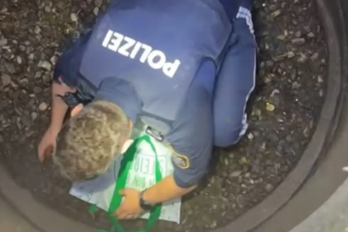 Ein Polizist in blauer Uniform kniet in einem Schacht mit Kieselsteinen und hält eine grüne Tasche mit Schriftzug.