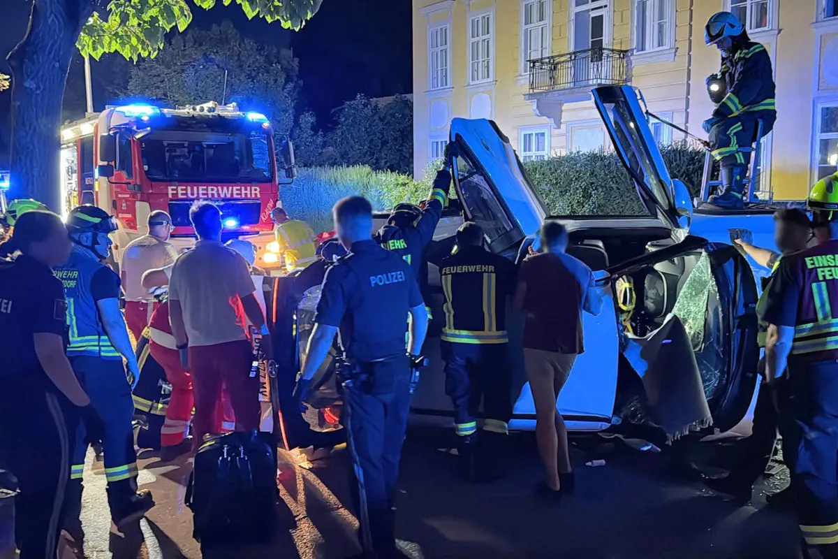Mehrere Feuerwehrleute und Polizisten stehen um ein verunfalltes Auto, das auf der Seite liegt. Ein Feuerwehrauto ist im Hintergrund sichtbar.