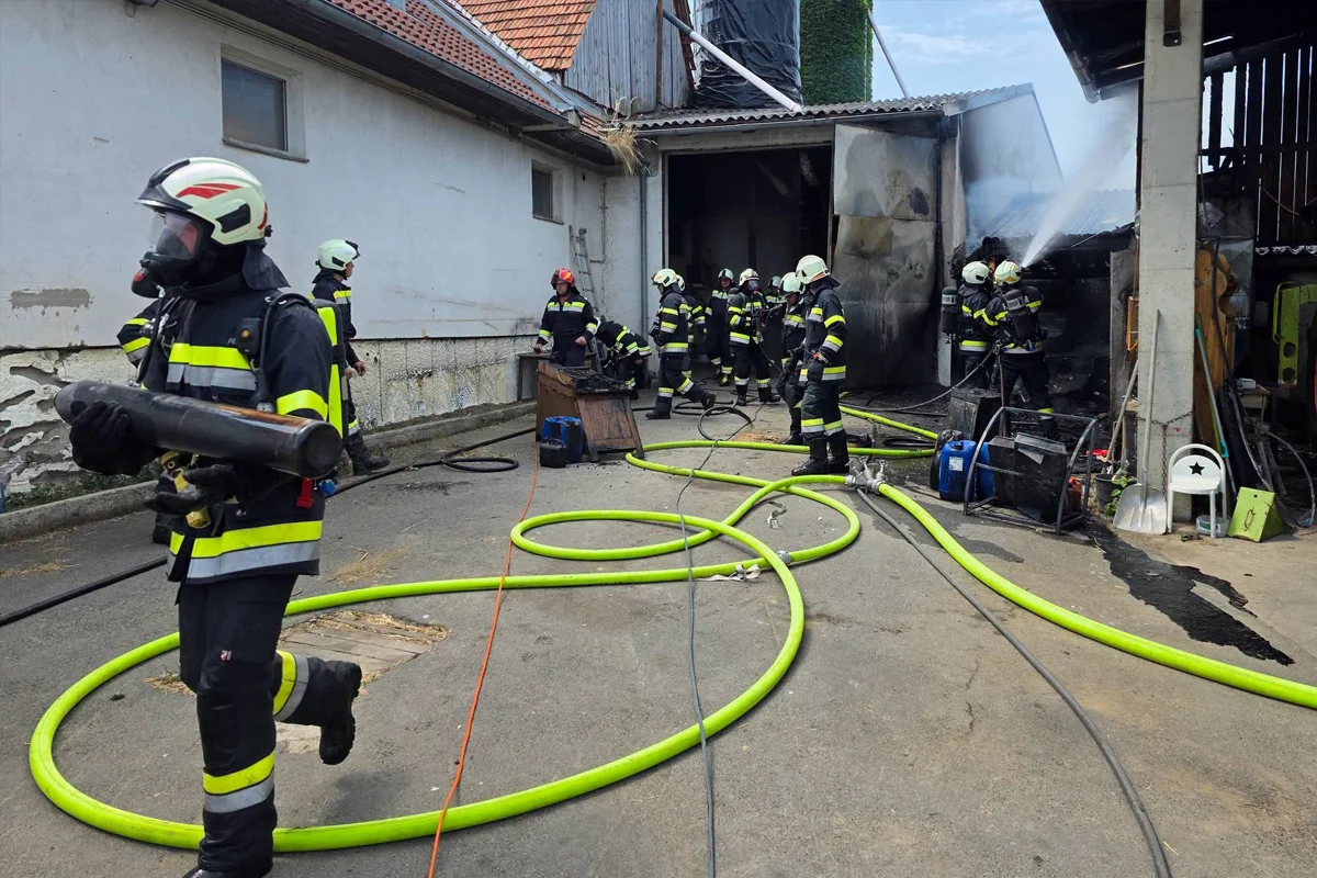 Mehrere Feuerwehrleute in Schutzkleidung löschen einen Brand in einem offenen Gebäude mit gelben Schläuchen und Einsatzgeräten.