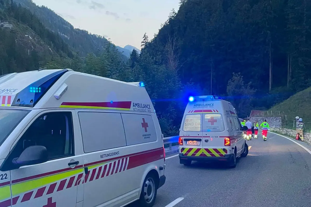 Auf einer kurvenreichen Bergstraße stehen zwei Ambulanzfahrzeuge mit aktiviertem Blaulicht. Im Hintergrund sind mehrere Einsatzkräfte in Warnwesten sichtbar.