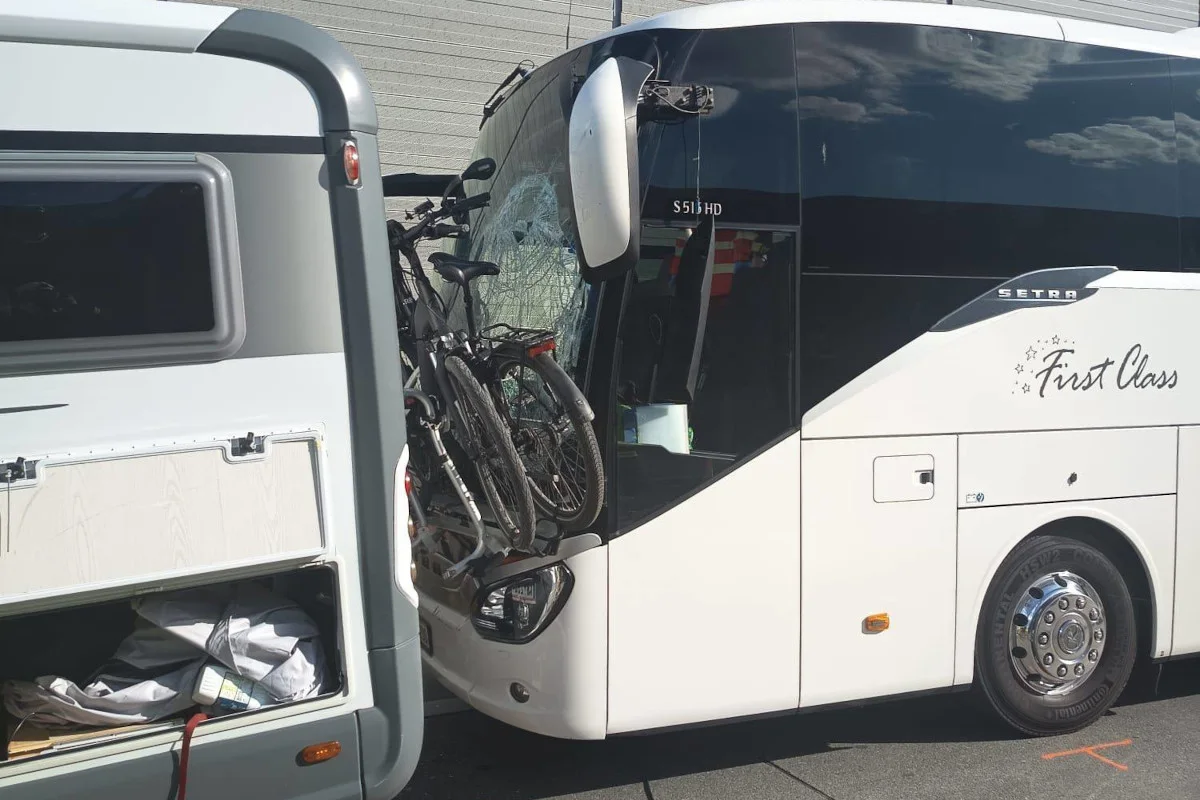 Ein weißer Reisebus hat eine beschädigte Frontscheibe mit zwei Fahrrädern, die darauf montiert sind. Daneben steht ein geöffneter Wohnwagen.