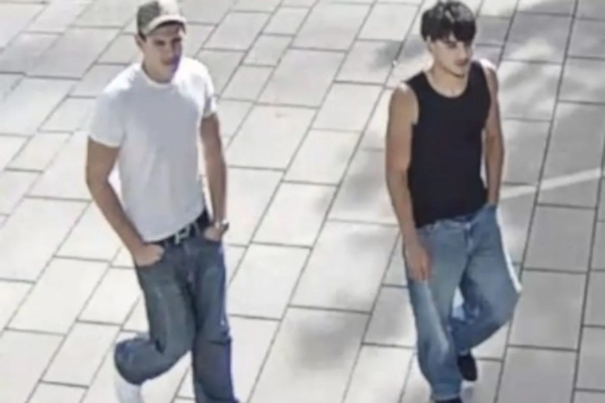 Zwei junge Männer in Freizeitkleidung gehen nebeneinander auf einem gepflasterten Weg. Einer trägt ein weißes T-Shirt, der andere ein schwarzes Tanktop.