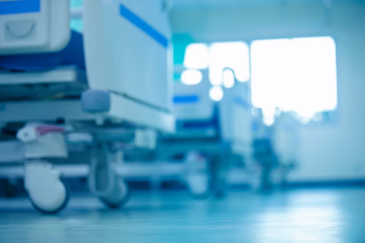 Das Bild zeigt eine unscharfe Ansicht von Krankenhausgeräten oder Betten in einem hell erleuchteten Raum.