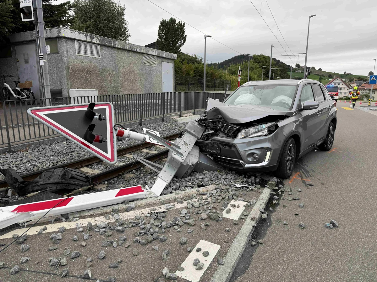 Ein grauer SUV ist in eine Bahnschranke gefahren, die Schiene liegt in einer städtischen Umgebung. Der Vorderteil des Autos ist stark beschädigt.