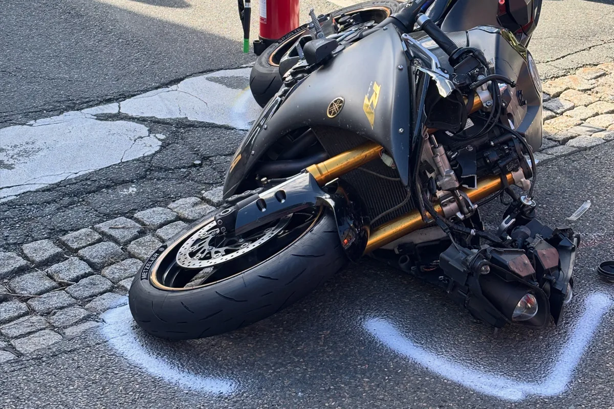 Ein beschädigtes Motorrad liegt auf der gepflasterten Straße. Das Vorderrad ist deutlich sichtbar und zeigt Schäden.