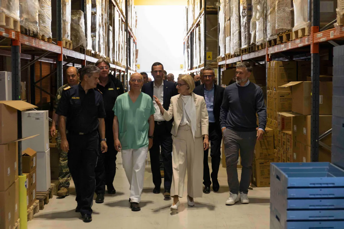 Eine Gruppe von Personen, darunter Polizisten in Uniform, geht durch ein Lager mit hohen Regalen voller Kartons.