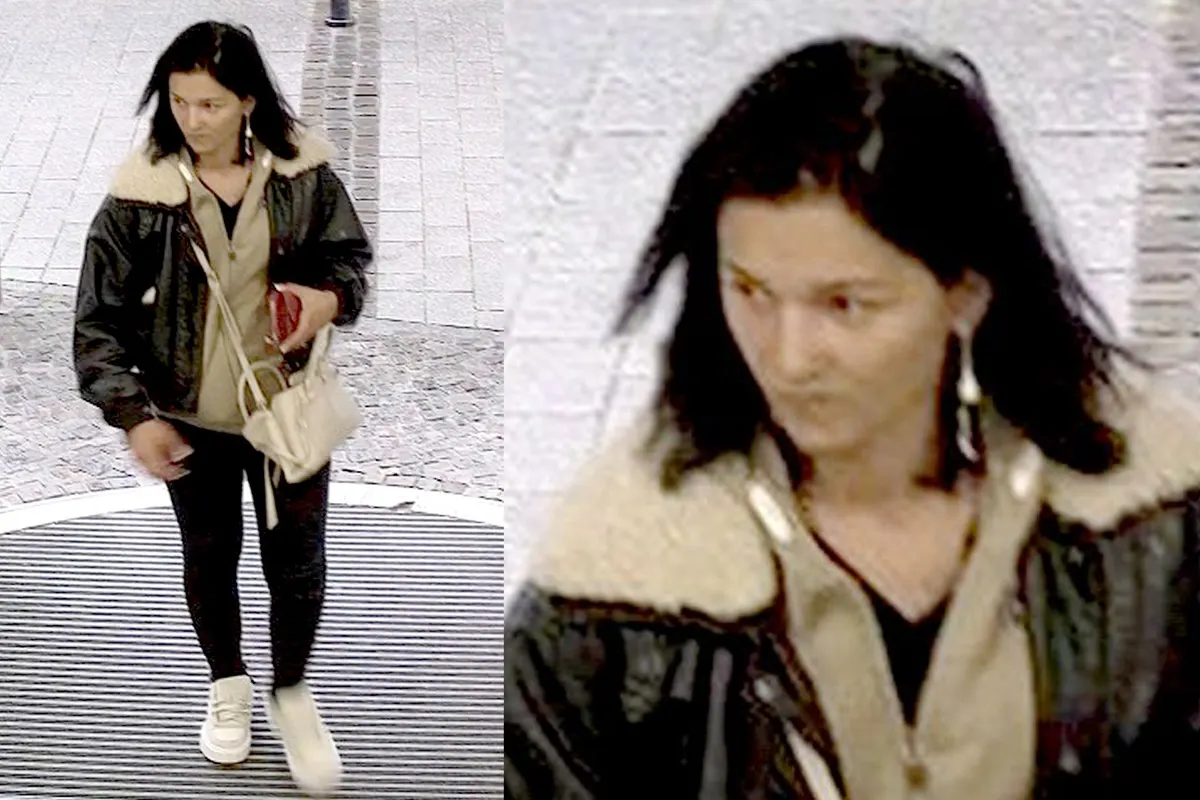 Eine Frau mit dunklem Haar trägt eine dunkle Jacke mit hellem Kragen und hält eine helle Handtasche, während sie durch einen Eingang geht.