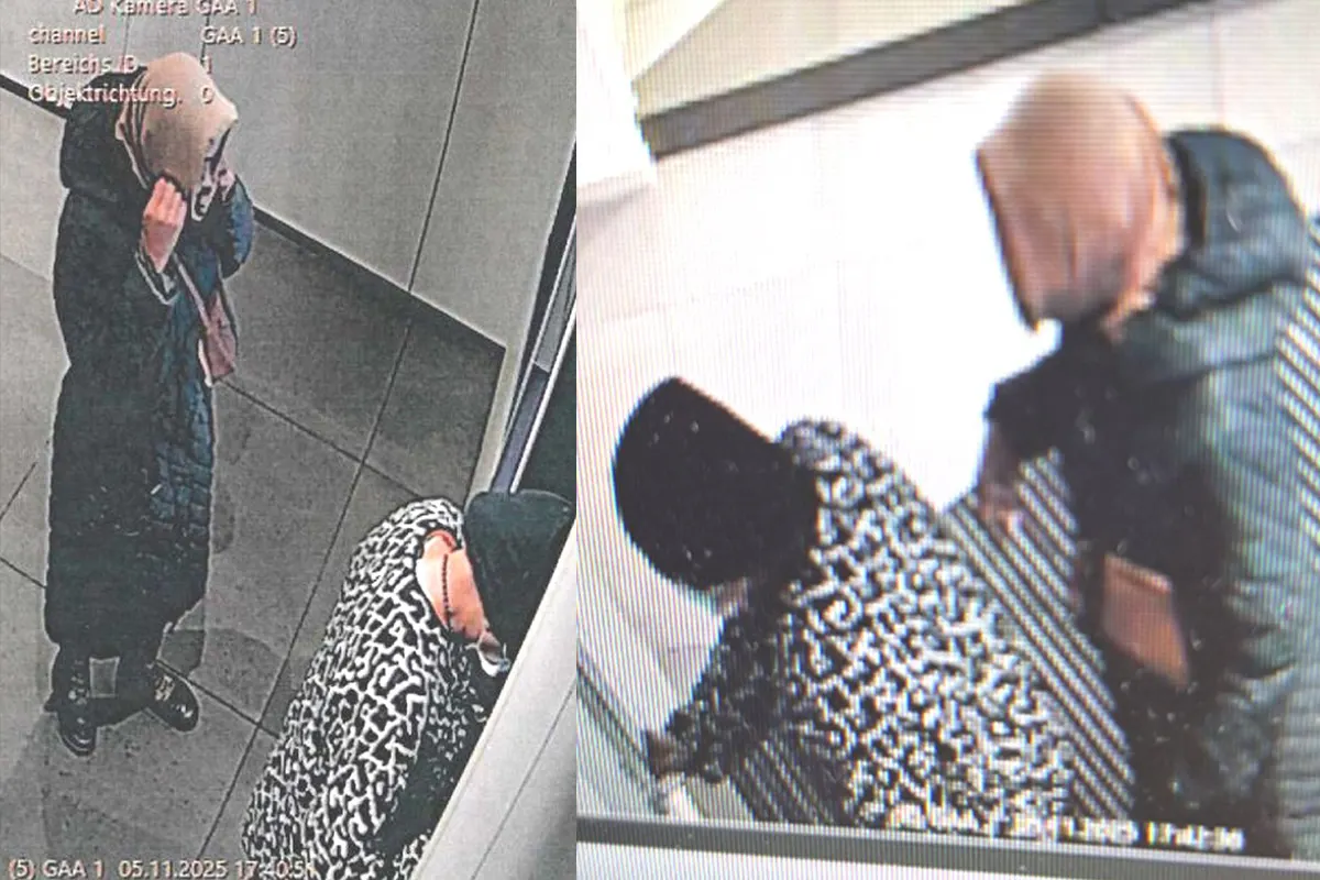 Eine Person in einem dunklen Mantel steht an einem Geldautomaten, während eine andere daneben steht. Beide Personen sind vermummt.