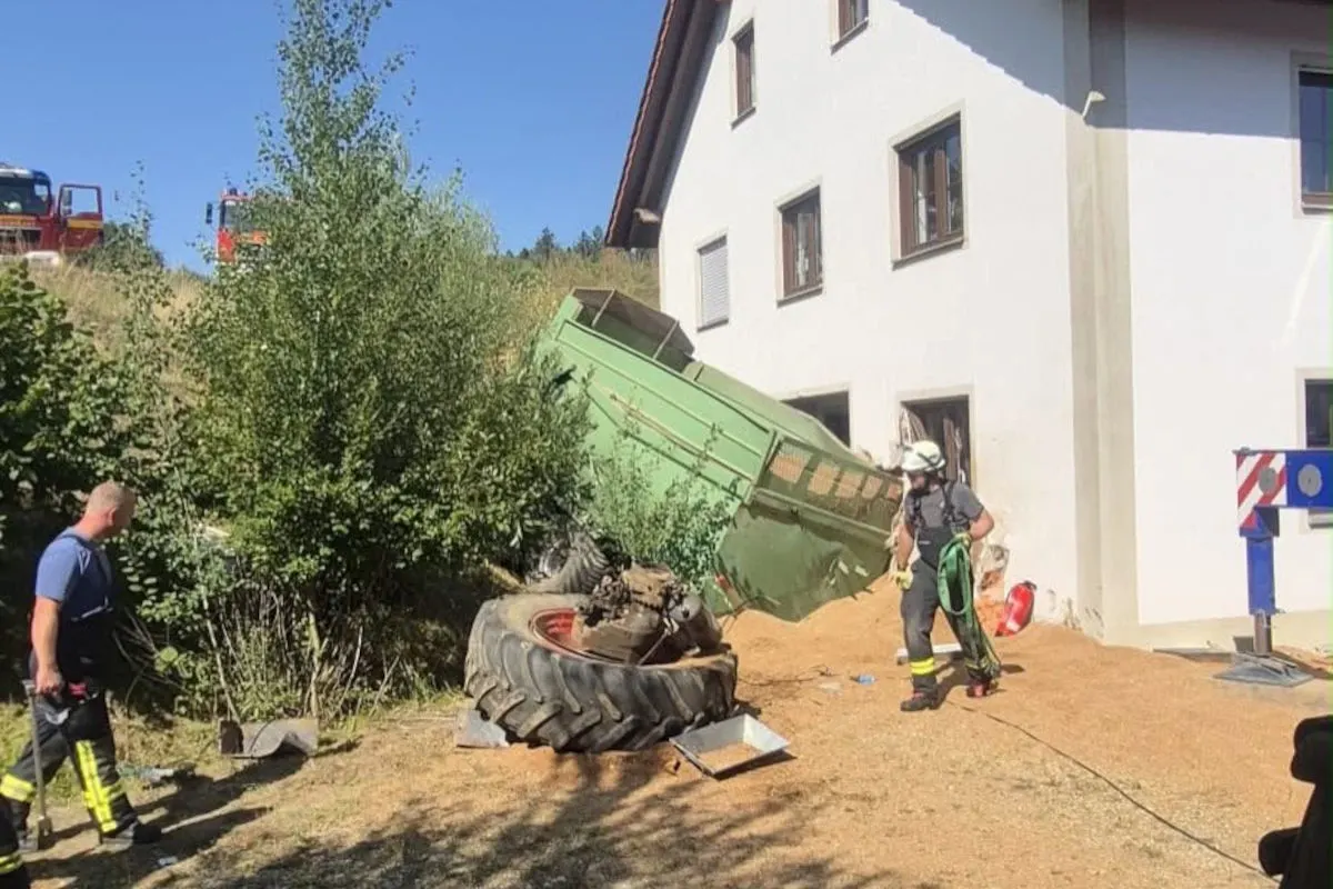 Ein grüner Anhänger liegt umgekippt vor einem mehrstöckigen Gebäude. Feuerwehrleute sind vor Ort, um die Lage zu sichern.